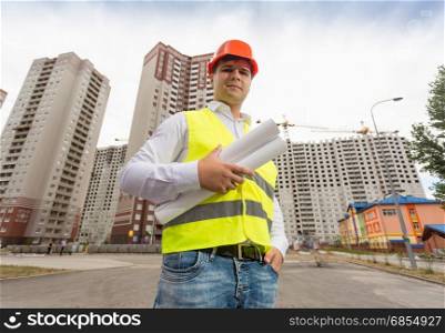 Portrait of construction engineer in hardhat posing in front of just built buildings