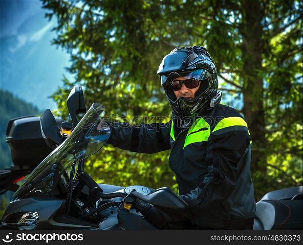 Portrait of cool biker on beautiful nature background, handsome man driving motorcycle, extreme sport, travel along Europe, joy and freedom concept