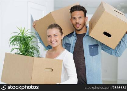 portrait of couple in apartment carrying cardboard boxes
