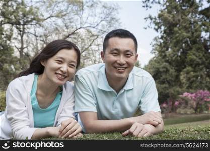 Portrait of couple lying in grass in park.