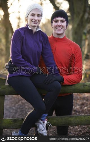 Portrait Of Couple On Winter Run Through Woodland Sitting On Fence