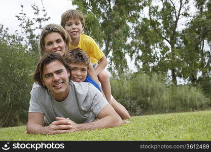 Portrait of couple with two sons (6-11) lying on top of each other on lawn