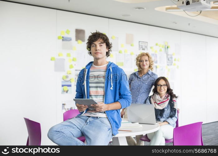 Portrait of creative businessman holding digital tablet with female colleagues in background