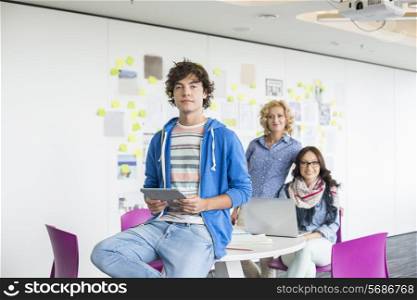 Portrait of creative businessman holding digital tablet with female colleagues in background