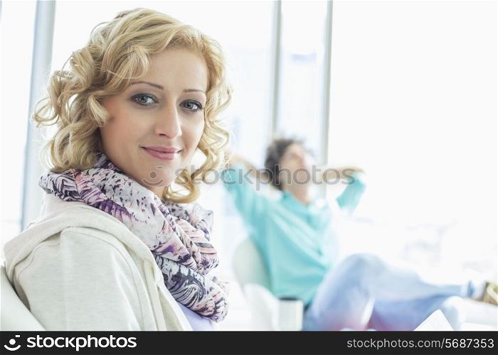 Portrait of creative businesswoman at lobby with colleague relaxing in background