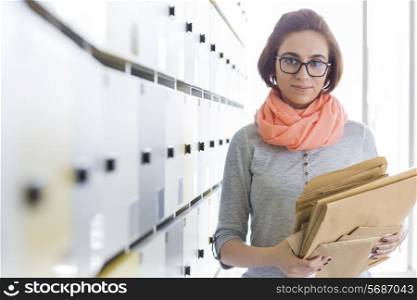 Portrait of creative businesswoman holding envelopes in locker room at office