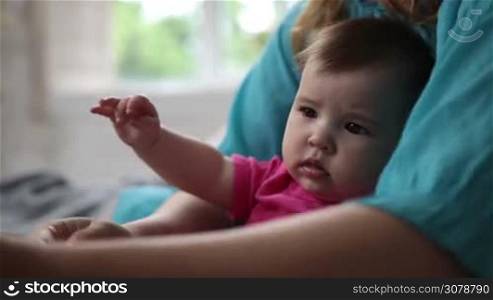 Portrait of curious baby girl smelling tulip flower while sitting on mother&acute;s lap. Closeup. Adorable infant child playing with flower and discovering the world while relaxing in mother&acute;s loving embrace. Slow motion. Steadicam stabilized shot.