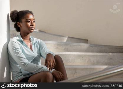 Portrait of curly hair woman sitting on steps and staircases and looking away.