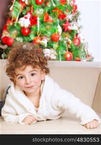 Portrait of cute adorable little boy lying down on the couch near beautiful decorated Christmas tree, spending winter holidays at home