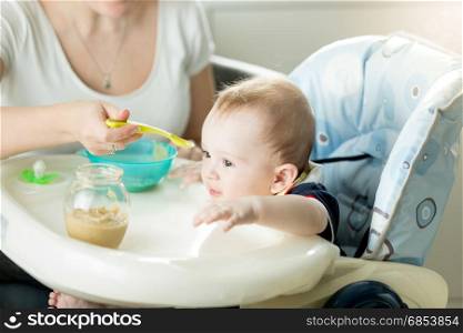 Portrait of cute adorably baby boy sitting in chair and eating from spoon