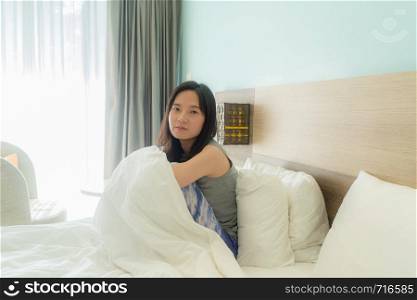 Portrait of cute Asian woman looking at camera on bed in a modern bedroom with white blanket.