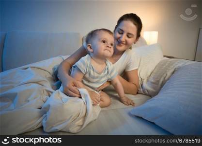 Portrait of cute baby boy and his mother in bed at late night