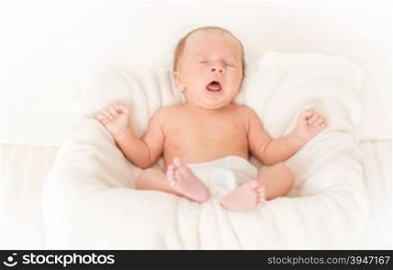 Portrait of cute baby boy lying in bed and yawning