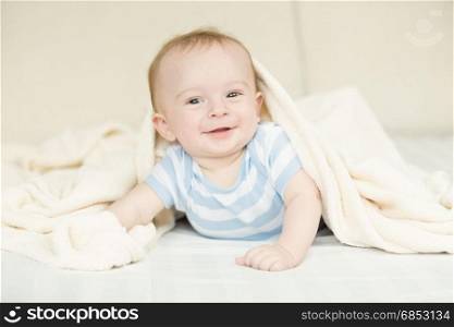 Portrait of cute baby boy lying under blanket
