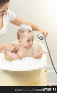 Portrait of cute baby boy playing in bath with shower head