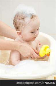 Portrait of cute baby boy playing in foam bath with yellow rubber duck