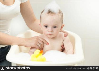 Portrait of cute baby boy playing with yellow rubber duck in bath