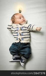 Portrait of cute baby boy posing on bed with glowing light bulb overhead