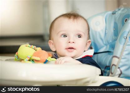 Portrait of cute baby boy sitting in child chair with table