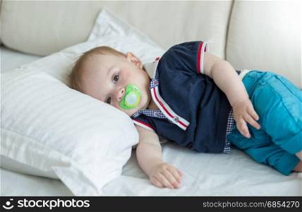 Portrait of cute baby boy with soother lying on bed