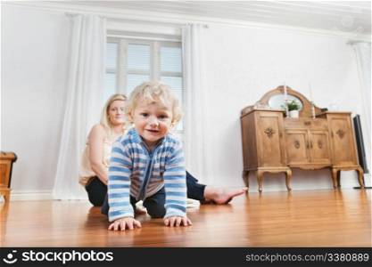 Portrait of cute baby crawling on the floor with mother in the background