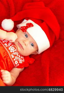 Portrait of cute baby girl wearing red Santa Claus hat with bow lying down in the bed at home, New Year party for children