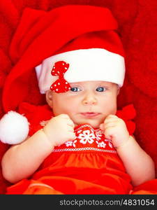 Portrait of cute baby girl wearing red Santa Claus hat with bow lying down in the bed at home, New Year party for children