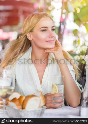 Portrait of cute blond female drink water with lemon in nice outdoor European cafe, healthy lifestyle, enjoying wonderful summer traveling to Italy