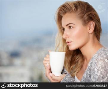 Portrait of cute blond female drinking tea on the outdoors terrace, having breakfast at home, feeling pleasure and relaxation