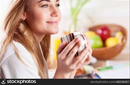 Portrait of cute blond female having coffee in the kitchen, enjoying happy lazy morning, peace and relaxation at home