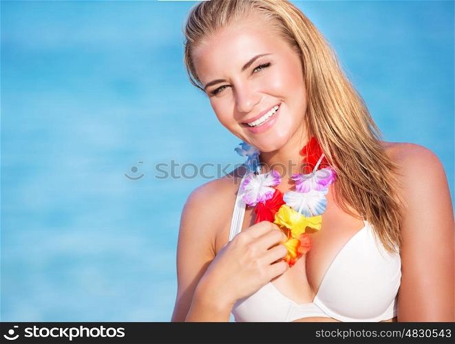 Portrait of cute blond female wearing beautiful Hawaiian leis, having fun on the beach, tropical party with traditional flowers garland on neck&#xA;