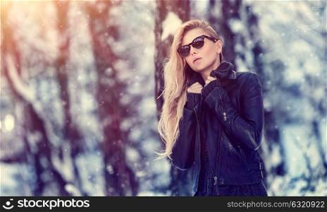 Portrait of cute blond female wearing stylish sunglasses and leather jacket in winter park, cool street fashion