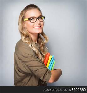 Portrait of cute blond student girl over gray background, wearing glasses and holding in hands colorful books, back to school