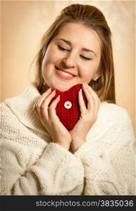 Portrait of cute blonde woman embracing red knitted heart