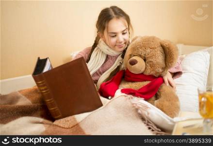Portrait of cute brunette girl telling story to teddy bear at bed