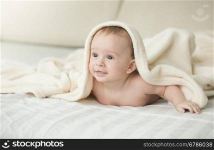 Portrait of cute cheerful baby lying under blanket on bed