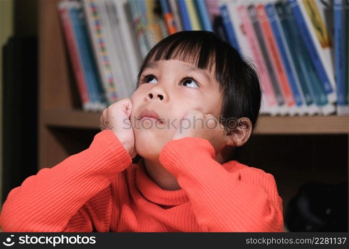 Portrait of cute child looking up and thinking with hands on chin in living room. school child thinking
