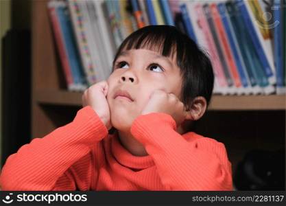 Portrait of cute child looking up and thinking with hands on chin in living room. school child thinking