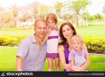 Portrait of cute family in spending time together in the park, happy young parents with two adorable child outdoors, love concept