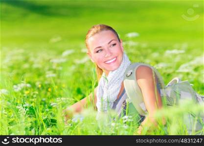 Portrait of cute female sitting on floral field, happy traveler with backpack resting outdoors, summer vacation concept