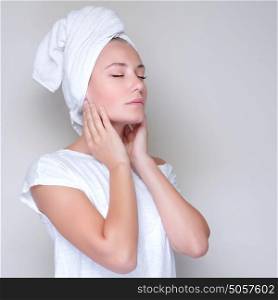 Portrait of cute female with closed eyes and towel on head touching face, studio shot, applying facial cream, pampering and health care concept