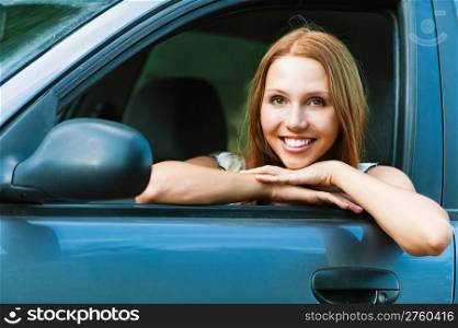 Portrait of cute, fun, young woman sitting in the car looking out the window, leaning on the arm