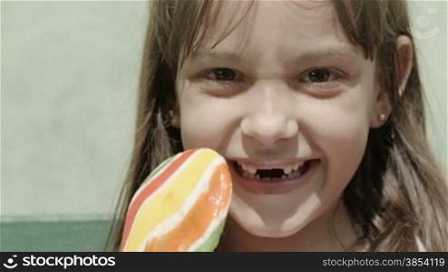 Portrait of cute gap-toothed female child with lollipop smiling and looking at camera