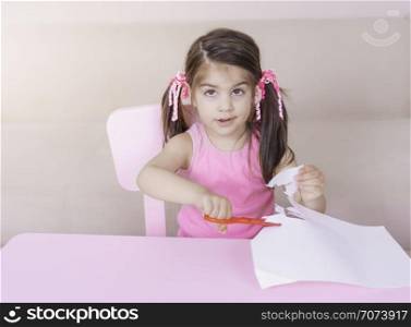 Portrait of Cute girl cutting paper alone with scissors while sitting at table Selective focus and small depth of field.. Portrait of Cute girl cutting paper alone with scissors