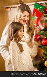 Portrait of cute girl decorating Christmas tree with mother