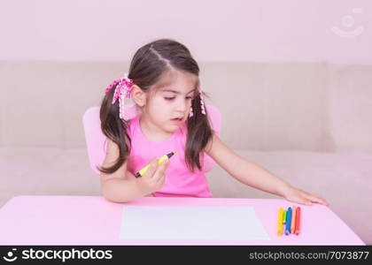 Portrait of Cute girl drawing with colorful pencils on white paper sitting at table. Selective focus and small depth of field.. Portrait of Cute girl drawing with colorful pencils
