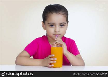 Portrait of cute girl drinking orange juice against colored background