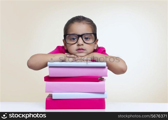 Portrait of cute girl leaning on stack of books against colored background