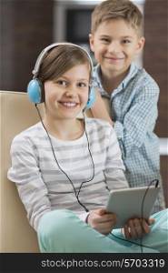 Portrait of cute girl listening music on digital tablet while brother standing behind her