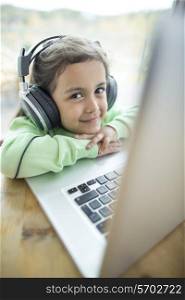 Portrait of cute girl listening to music on headphones while using laptop at home